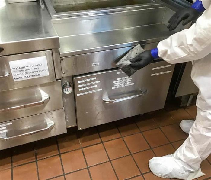 Employee cleaning commercial kitchen equipment. 